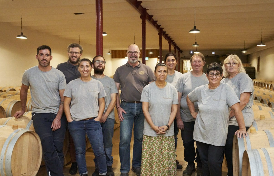 Group of people posing together in a winery with wine barrels in the background
