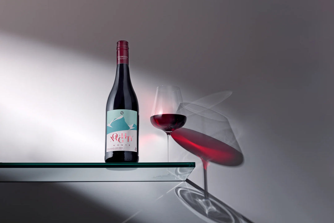 Wine bottle and glass on a reflective surface with a gray background