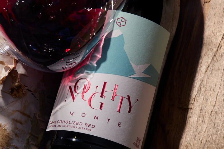 Wine bottle labeled 'Nughty Monte' with a glass of red wine on a wooden surface.