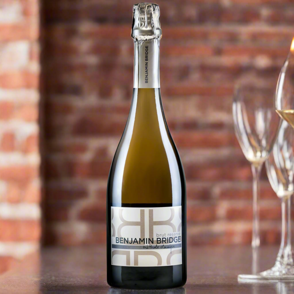 Benjamin Bridge Brut Reserve sparkling wine bottle displayed with wine glasses against a rustic brick background, highlighting this premium Canadian wine crafted in the traditional method