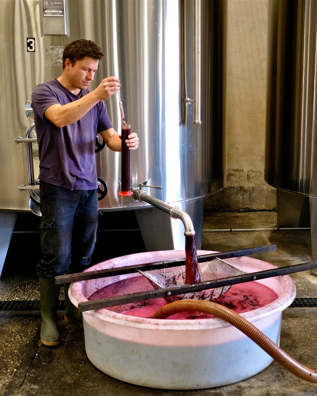 Winemaker sampling red wine during fermentation at Vignobles Gabriel cellar