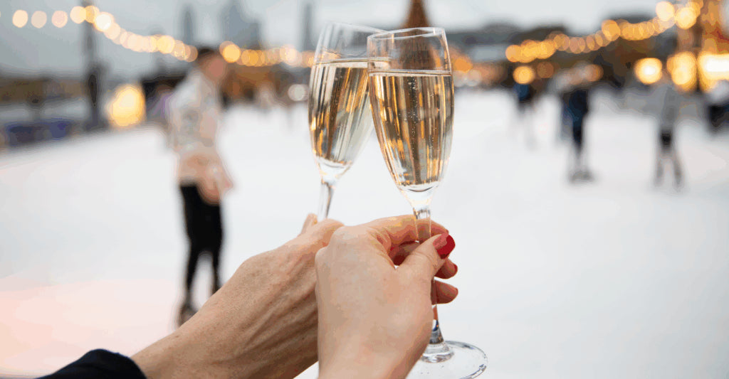 Two champagne glasses being clinked together with a blurred ice rink and people in the background.