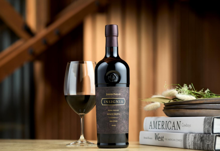 Wine bottle labeled 'Insignia' with a glass of wine on a wooden table.